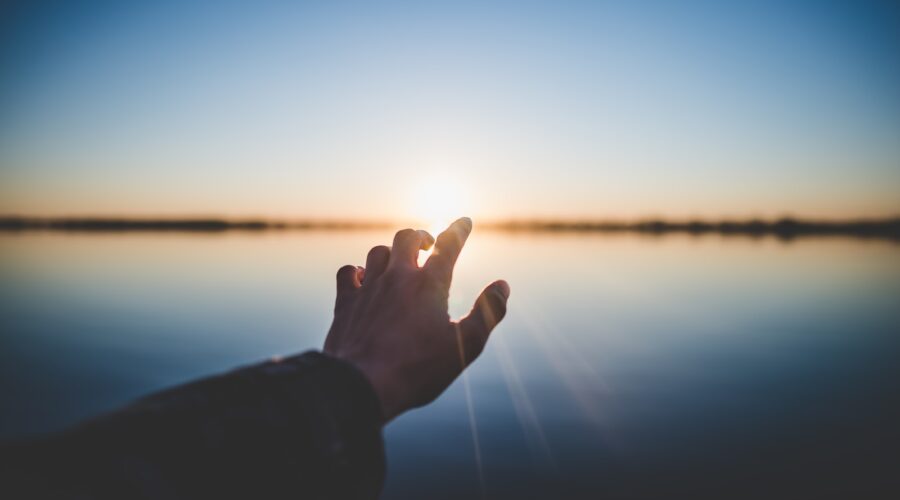 landscape photography of person's hand in front of sun