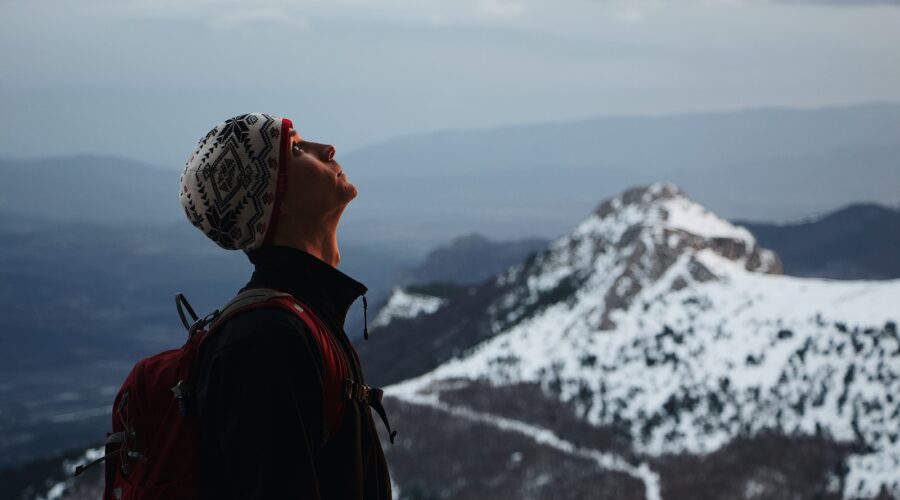 man wearing black jacket with red backpack standing while looking up