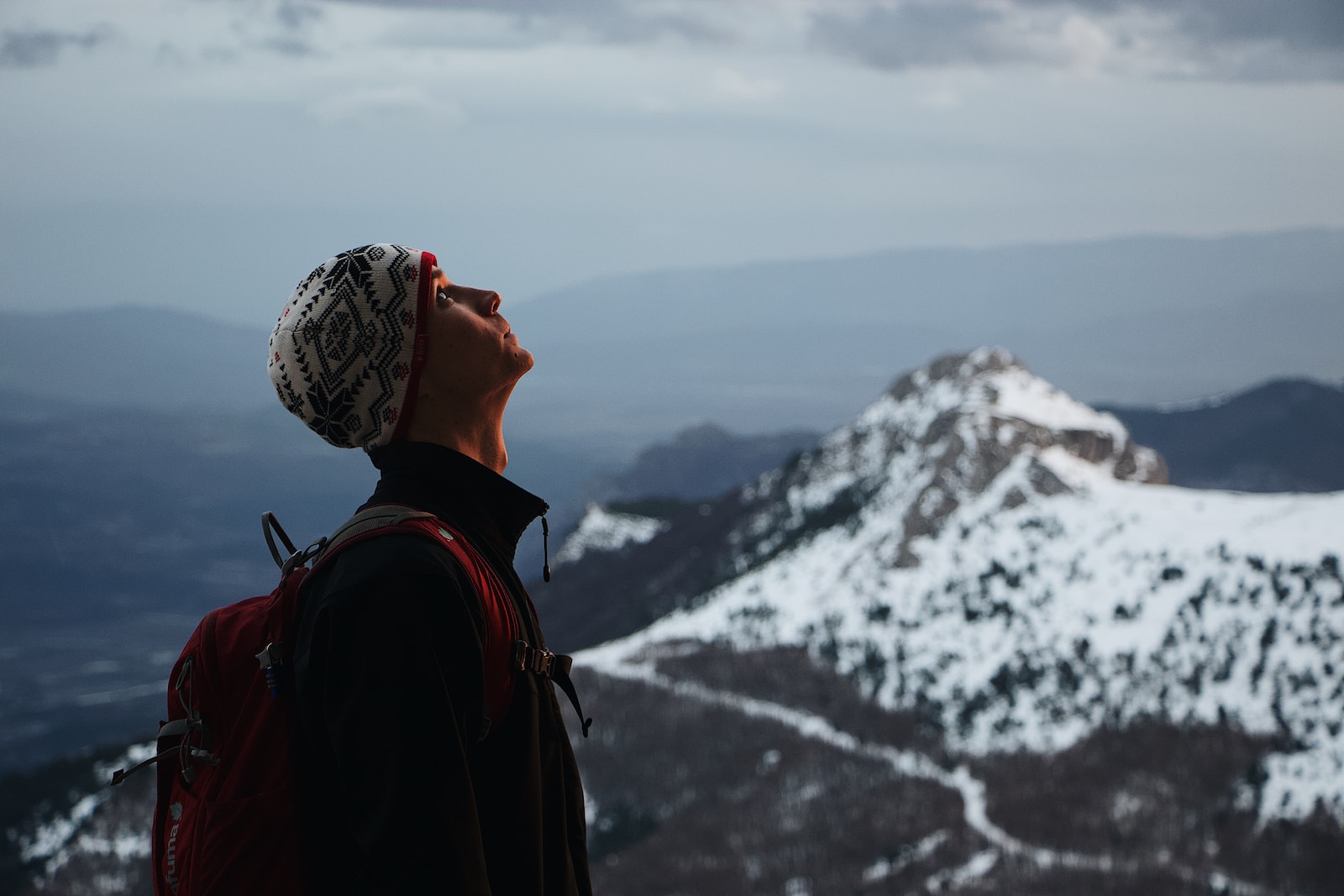 man wearing black jacket with red backpack standing while looking up