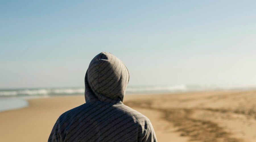 person wearing gray hooded top facing seashore