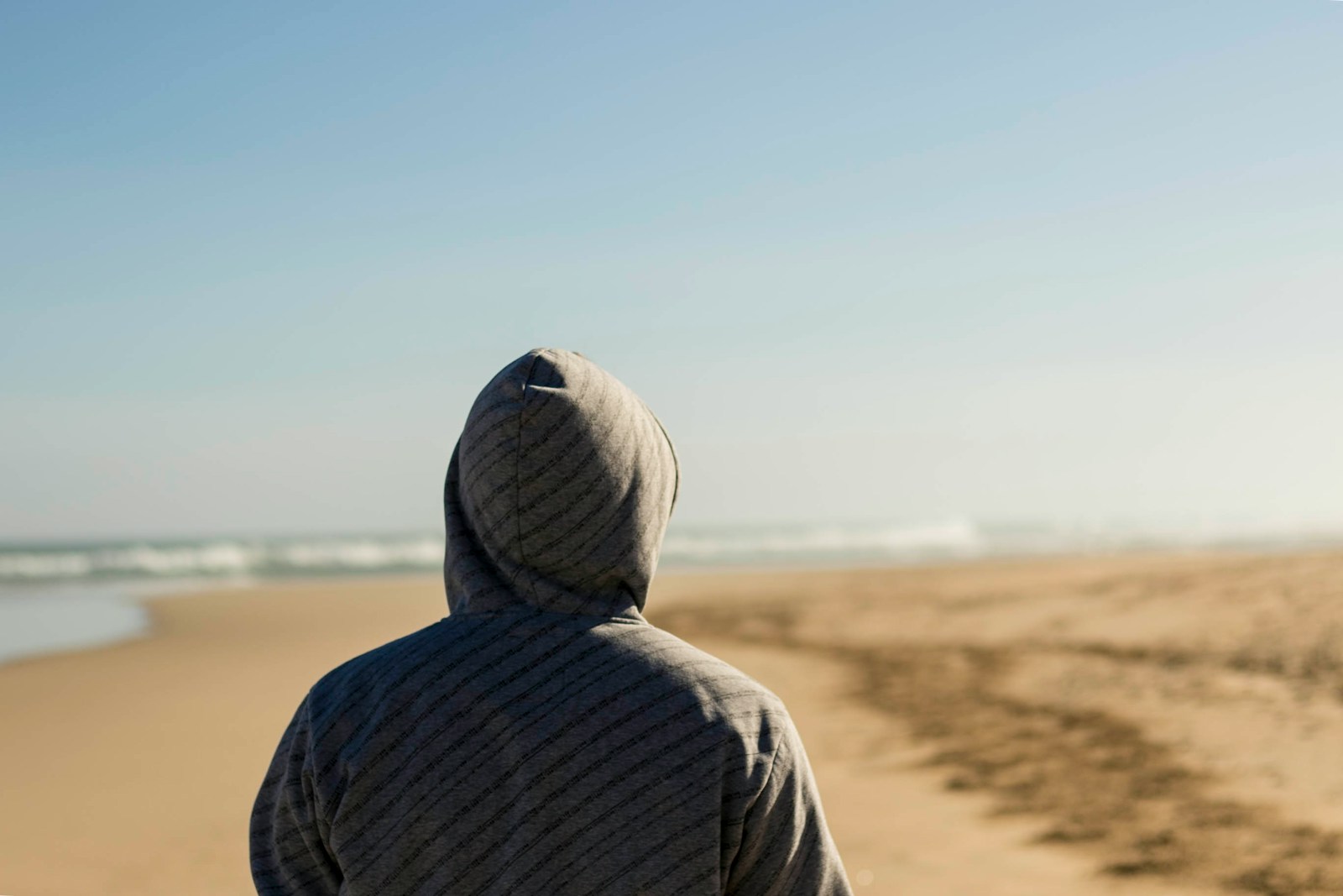 person wearing gray hooded top facing seashore