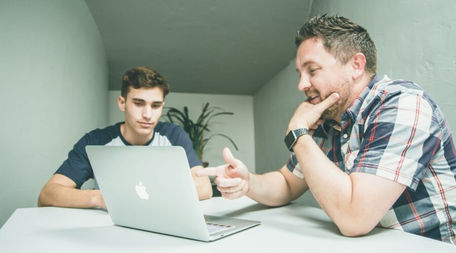 man wearing white and black plaid button-up sports shirt pointing the silver MacBook