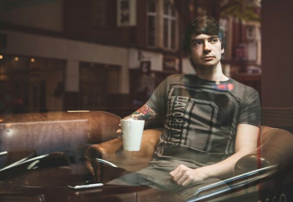 man sitting on beige armchair while holding white ceramic mug