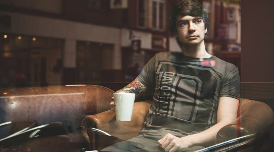 man sitting on beige armchair while holding white ceramic mug