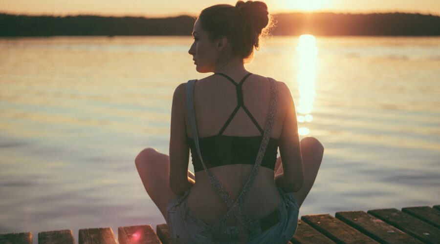 woman sitting on brown wooden dock during sunset