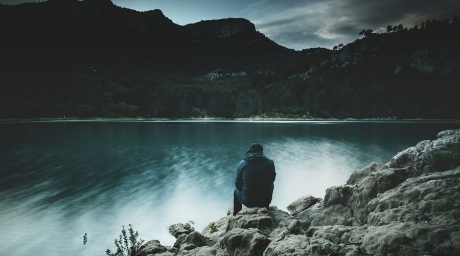 a man sits on a rock staring across a lake at dusk